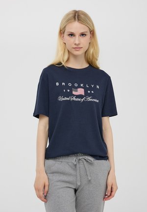 T-shirt in cotone navy con la scritta "BROOKLYN" e un piccolo design della bandiera americana, abbinato a pantaloni della tuta grigi con coulisse.