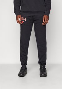 Pantaloni da jogging neri in misto cotone, con polsini a coste, tasche laterali e un logo rosso "BULLS" con una grafica di testa di toro sulla coscia sinistra.