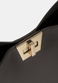 Sac à main en cuir noir avec un fermoir métallique doré à design géométrique et une texture lisse. Vue intérieure montrant l'ouverture.