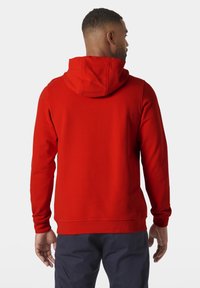 Sudadera roja con capucha ajustable, mangas largas, textura suave y puños y bajo de canalé. Detalles de costura visibles en la parte posterior.