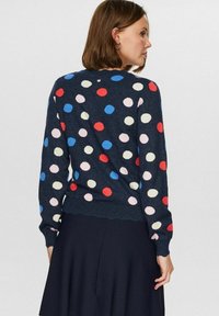 Mornarsko moder pulover z večbarvnimi pikami v rdeči, roza in modri barvi. Ima okroglo ovratnico ter rebraste manšete in rob.