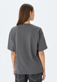 Grijze oversized t-shirt, korte mouwen, ronde halslijn, van katoen. Minimalistisch ontwerp zonder patronen, wordt van de achterkant getoond.
