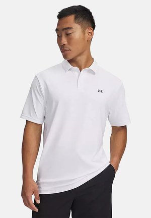 Hombre con una camiseta polo de manga corta blanca con un pequeño logo negro en el pecho y pantalones negros, mirando hacia un lado.