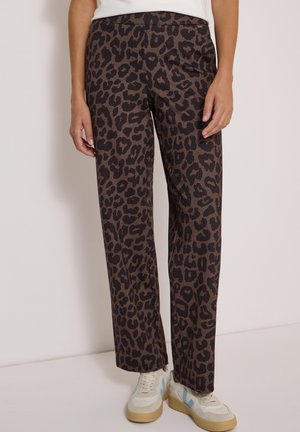 Pantalon large à imprimé léopard porté avec des baskets blanches et un haut blanc sur un fond uni.