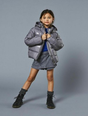Chaqueta de plumón gris con capucha, acabado brillante, cremallera frontal, usada sobre un suéter azul y una falda de mezclilla, combinada con botas negras de cordones.