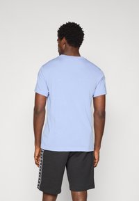 T-shirt azul claro de gola redonda com mangas curtas, feita de um tecido misto de algodão. Combinada com calções pretos que apresentam uma marcação lateral.
