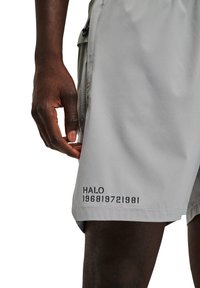 Ljusgrå shorts i syntetmaterial, med en svart tryckt logotyp "HALO" med siffror på nedre vänstra sidan.