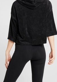 Hoodie noir court en tissu doux et texturé avec capuche, coupe ample et manches courtes, associé à des leggings noirs.