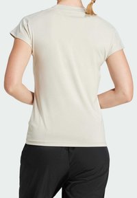 Beige t-shirt med kort ärm, slät textur, rund halsringning och figurnära design, kombinerad med svarta byxor. Inga synliga mönster eller grafik.