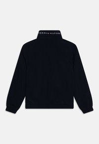 Black long-sleeve jacket with elastic cuffs, elastic waistband, and "Tommy Hilfiger" logo on the back collar.