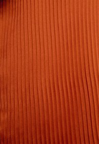 Tecido texturizado em cor terracota quente, com padrões verticais em relevo. A superfície parece suave e lisa, destacando a sua qualidade tátil.