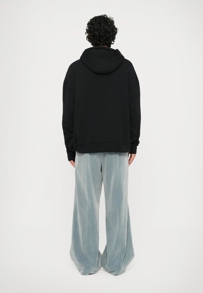 Zwarte hoodie met een relaxte pasvorm, geribde boorden en een trekkoordkap, gecombineerd met lichtblauwe wijde broek in een zachte stof.