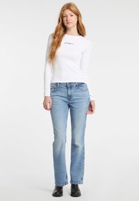 Top bianco a maniche lunghe con logo nero, abbinato a jeans chiari a zampa d'elefante. Tessuto morbido con texture in denim blu e dettagli di cucitura sottili.