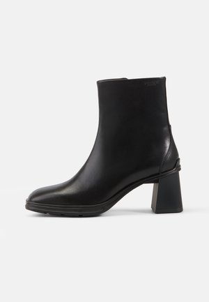 Musta nahkainen nilkkaboots, jossa on neliönmuotoinen kärki ja lohkokorko. Sujuva pinta ja selkeä muotoilu, vähäisillä koristeilla.