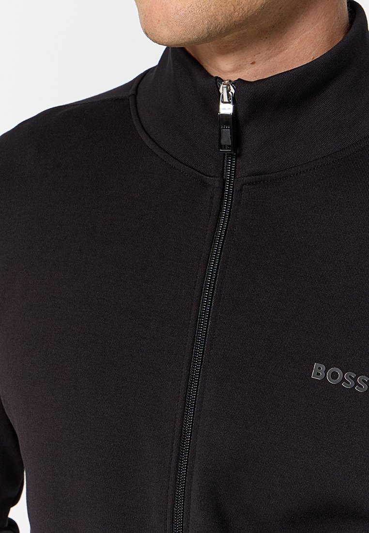 Giacca nera con zip e colletto alto, realizzata in tessuto liscia; presenta una zip metallica e un logo in rilievo discreto sul petto.