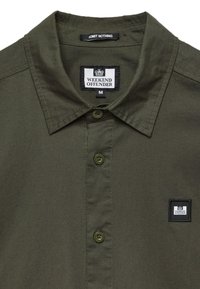 Olijfgroen overhemdd met een gladde stof. Beschikt over een kraag, twee knopen en een logo patch op de linkerborst.