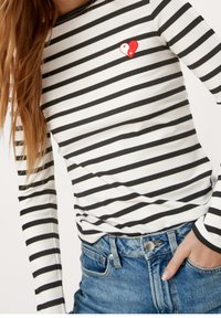 Długi top w paski z białej i czarnej prążkowanej tkaniny, z wyszytym na piersi czerwono-białym sercem yin-yang.