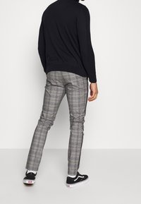 Zwart gebreid sweater en grijze geruite broek met blauwe accenten. De broek heeft een slim-fit, en de outfit is gecombineerd met zwarte sneakers.