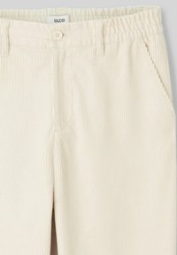 Pantalons en velours côtelé de couleur crème avec une surface texturée, taille élastique, fermeture à bouton et poches latérales.