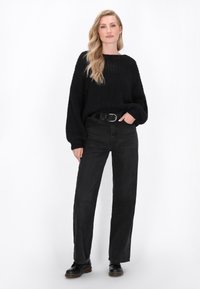 Pulover din tricot negru, cu o croială lejeră, decolteu rotund și model texturat, combinat cu blugi negri cu talie înaltă și cizme negre cu gleznă.