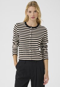Cardigan rayé noir et crème avec des manches longues et un col rond. Dispose d'une fermeture à boutons et de poignets côtelés. Texture en tricot douce.