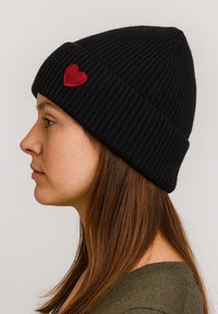 Black ribbed knit beanie with a small red heart patch on the side, worn snugly on a head, showcasing a simple and functional design.
