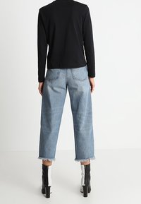 Un haut noir à manches longues associé à un jean large bleu clair avec des ourlets effilochés, porté avec des bottines à talons noires et blanches.