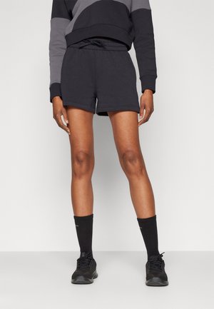 Person wearing black drawstring shorts, black crew socks, black athletic shoes, and a black and gray long-sleeve top against a plain background.