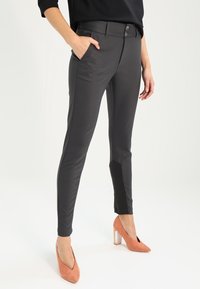 Slim-fit grå byxor med fickor, med en mjuk textur och kontrasterande svarta paneler vid ankeln, fastsatta med två knappar.