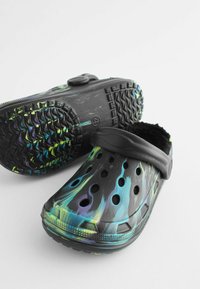 Sabots noirs avec un motif de flammes colorées en bleu et vert, comportant des trous de ventilation et une doublure en fausse fourrure douce. Comprend une sangle à l'arrière.