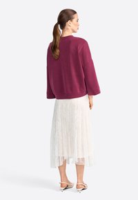 Felpa bordeaux con maniche larghe, abbinata a una gonna di pizzo bianco. L'outfit presenta intricati motivi in pizzo e un orlo dritto.