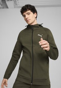 Olijfgroen ritsjack met capuchon, voorzien van een zwarte rits, gaasaccenten op de mouwen en een wit Puma-logo op de borst.