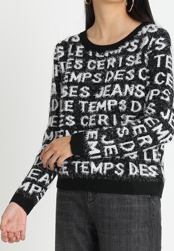 Pull en peluche noir et blanc avec un texte audacieux en motif répétitif, col rond, et poignets et ourlet côtelés noirs.