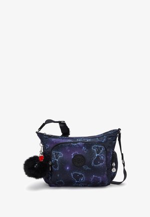 Tmavě modrá crossbody taška s hvězdnými vzory, s chlupatým černým pomponem na klíče a nastavitelným popruhem, umístěná na bílém pozadí.