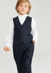 Mörkblå väst med fem knappar och framfickor, bärs över en vit skjorta. Skräddarsydda byxor fulländar den formella outfiten för ett barn.