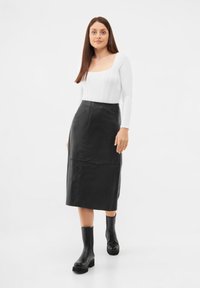 Musta nahkainen midi-hame, jossa on hyvin istuva vyötärö ja sileä pinta, yhdistettynä valkoiseen pitkähihaiseen paitaan ja mustiin chunky-saappaisiin.