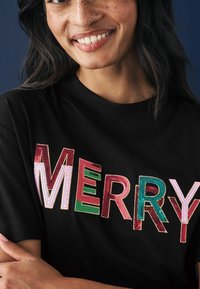 Čierne tričko s textúrovaným, viacfarebným nápisom "MERRY" s rôznymi vzormi. Krátke rukávy a okrúhly výstrih.