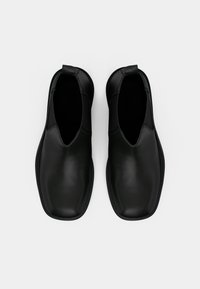 Pár černých kožených slip-on bot se čtvercovými špičkami a poutky, pohled z vrchu na bílém pozadí.