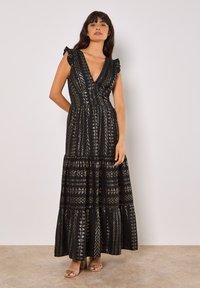 Robe maxi noire avec un décolleté en V profond, des manches à volants et des accents à motif métallique. Également dotée d'une jupe à volants et d'une taille cintrée.