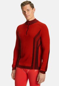 Pull en tricot rouge avec un col haut, fermeture éclair mi-hauteur à l'avant, et des rayures verticales noires contrastantes sur les côtés. Texture lisse et design ajusté.