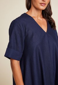 Marineblå linkjole med V-hals og rullede korte ærmer. Stoffet har en teksturert finish som fremhever en avslappet silhuett.