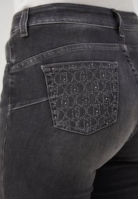 Jeans de mezclilla gris oscuro con un bolsillo trasero adornado con un patrón de pequeñas tachuelas metálicas. Corte estructurado, con cintura estándar.