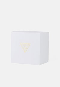 Hvit teksturert gaveeske med et gullfarget, trekantet GUESS-logo på forsiden. Esken har et minimalistisk design og rette kanter.
