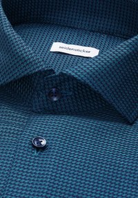 Blå textureret herreskjorte med mørke knapper og en hvid mærkelap syet ind i kraven med teksten "seidensticker".