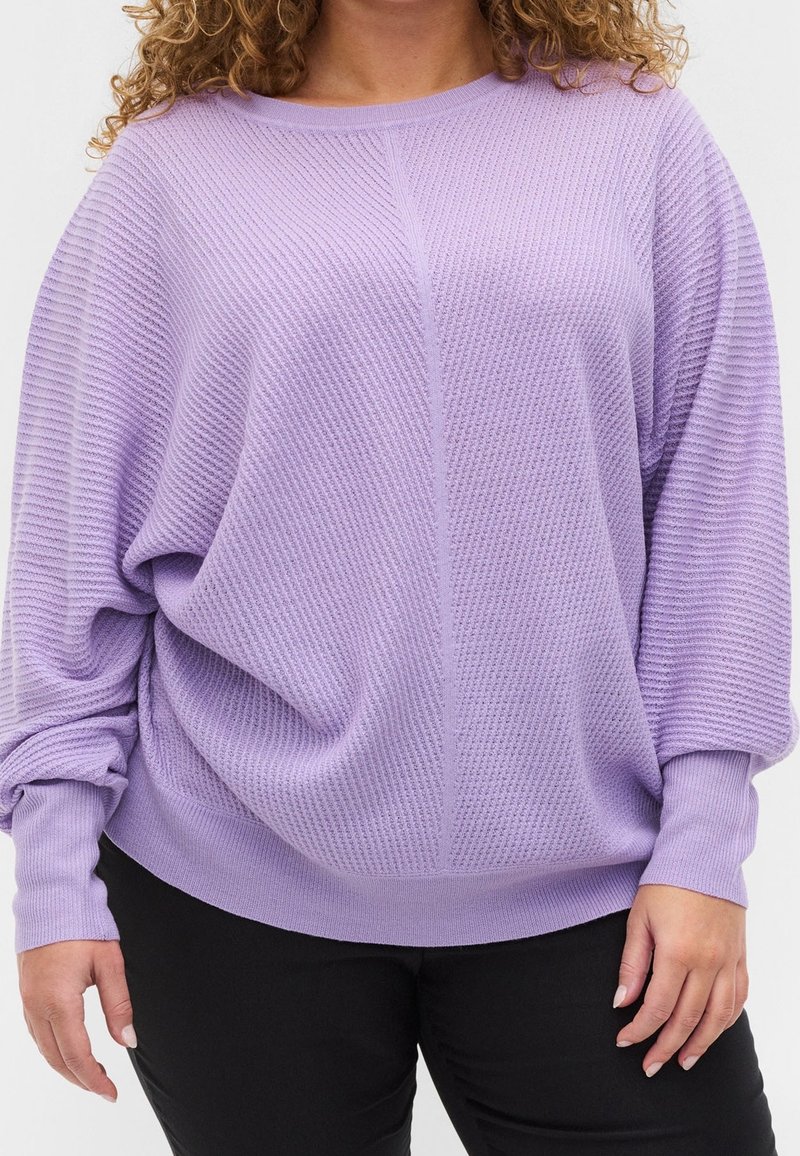 Lavendel strukturierter Pullover mit lockerer Passform, gerippten Details und langen Ärmeln, kombiniert mit schwarzen, körpernahen Hosen.