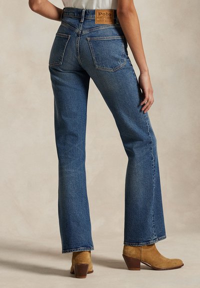 Osoba nosící modré džínsy s vysokým pasem, zadními kapsami a koženou značkou Polo, doplněné o hnědé kotníkové boty na podpatku.