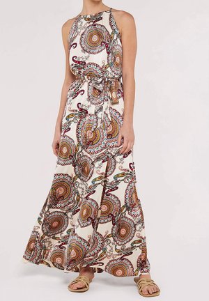 Femme portant une robe longue sans manches au sol avec des motifs circulaires colorés et paisley, associée à des sandales en corde beige.