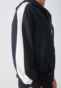 Zwarte zip-up hoodie met een witte streep langs de mouwen, van katoen, met een voorkantzak en geribbelde manchetten voor extra comfort.