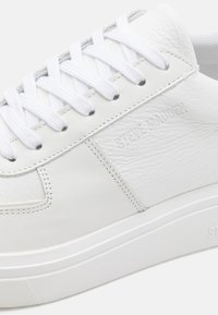 Baskets en cuir blanc avec panneaux texturés, dotées de lacets blancs et d'une semelle en caoutchouc. Nom de la marque « Steve Madden » embossé sur le côté.
