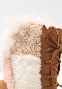 Beżowe i brązowe zamszowe botki z teksturowanymi futrzanymi panelami w kolorze różowym, kremowym i beżowym. Posiadają miękki futrzany kołnierz oraz sznurowane zapięcie z przodu.